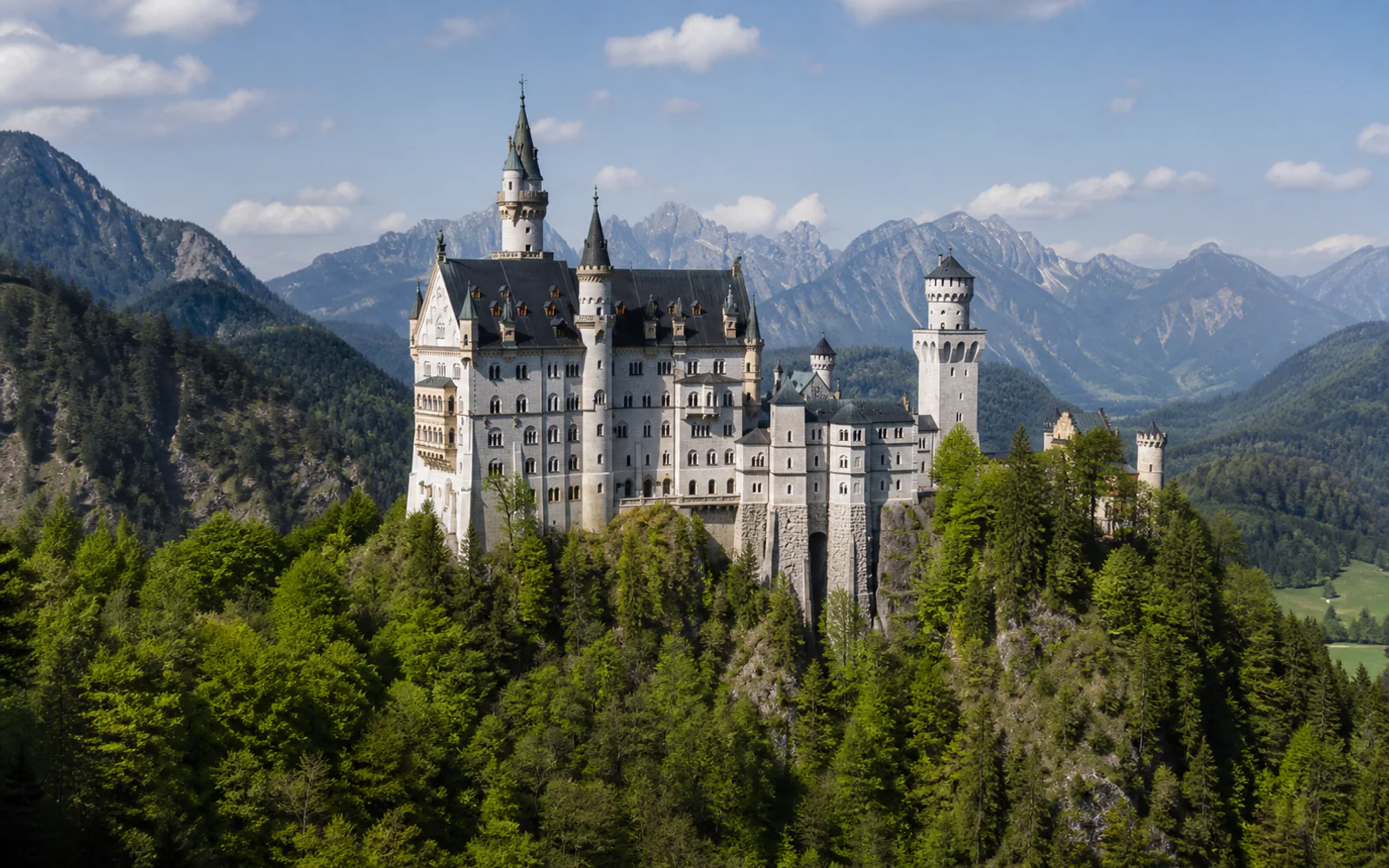 Neuschwanstein Castle above forested hills and the Bavarian Alps
