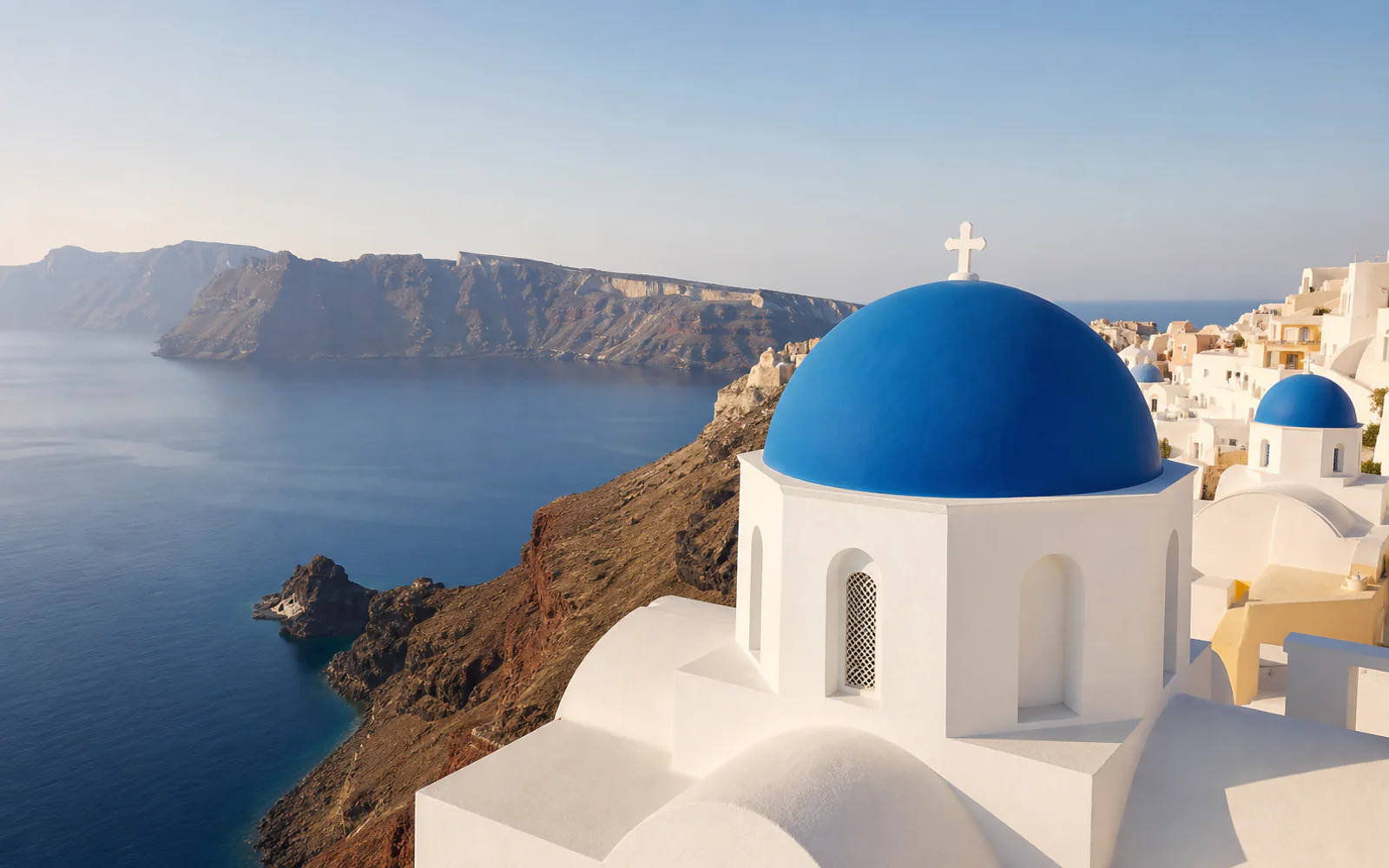 A blue-domed chapel overlooking Santorini’s volcanic caldera and the Aegean Sea