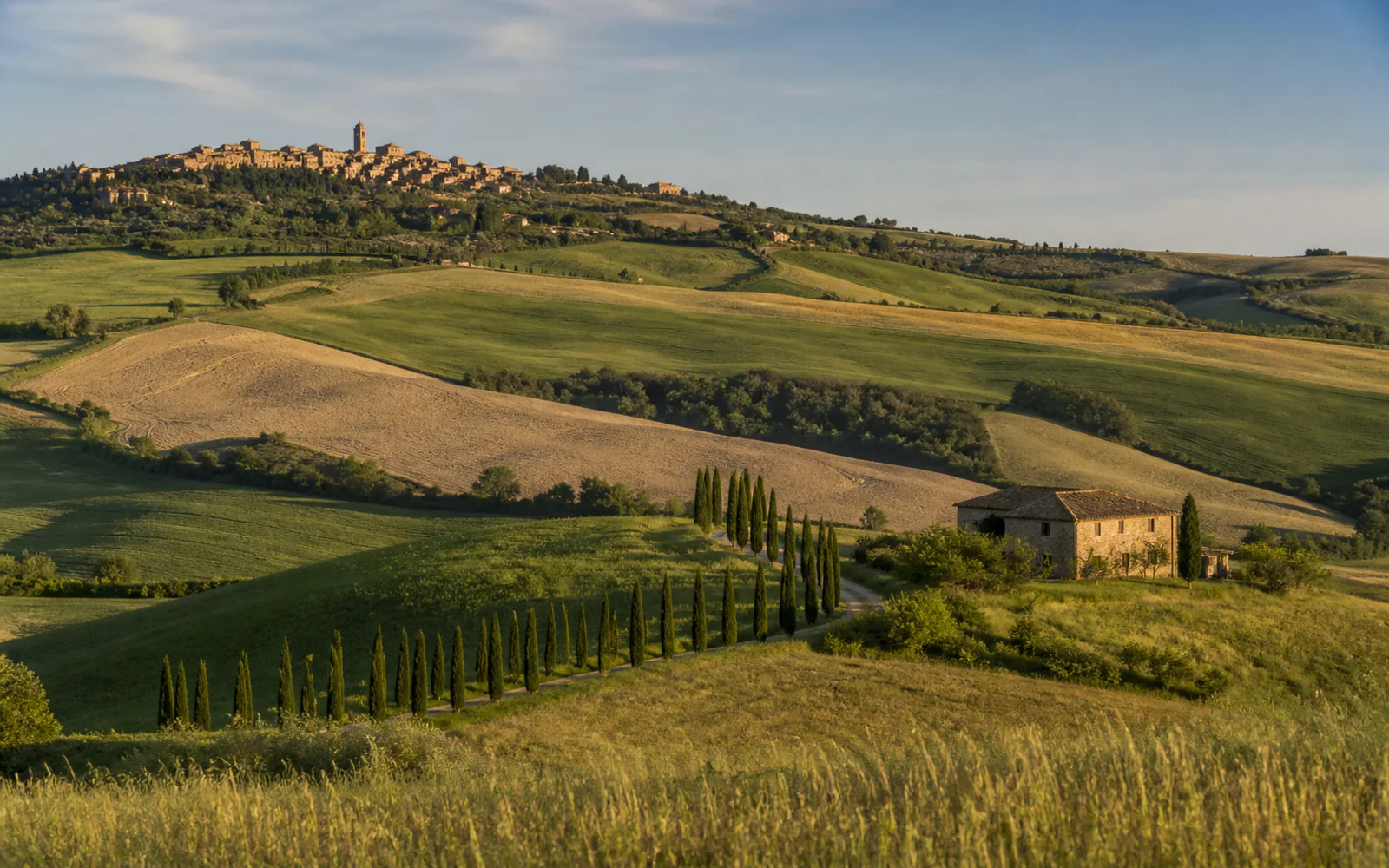 Cypress-lined road, stone farmhouse, and rolling hills in Tuscany’s Val d’Orcia